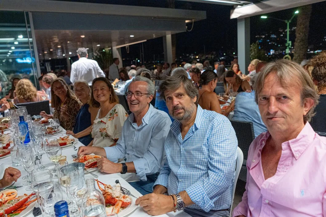 Grupo de personas en una cena en un restaurante al aire libre en la noche, con comida y bebidas en la mesa.