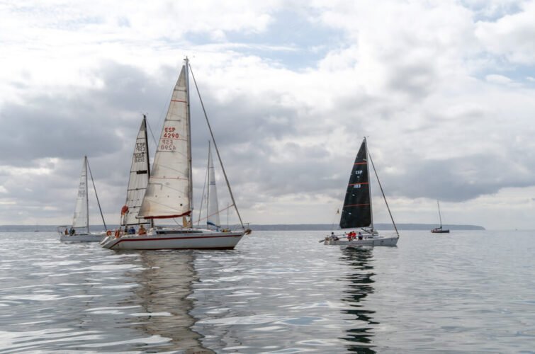 Tres barcos de vela navegando en aguas tranquilas bajo cielo nublado