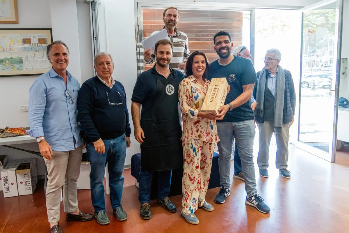 Un grupo de personas en una sala, con una mujer en el centro recibiendo una caja y sonriendo, mientras los demás observan y sonríen.