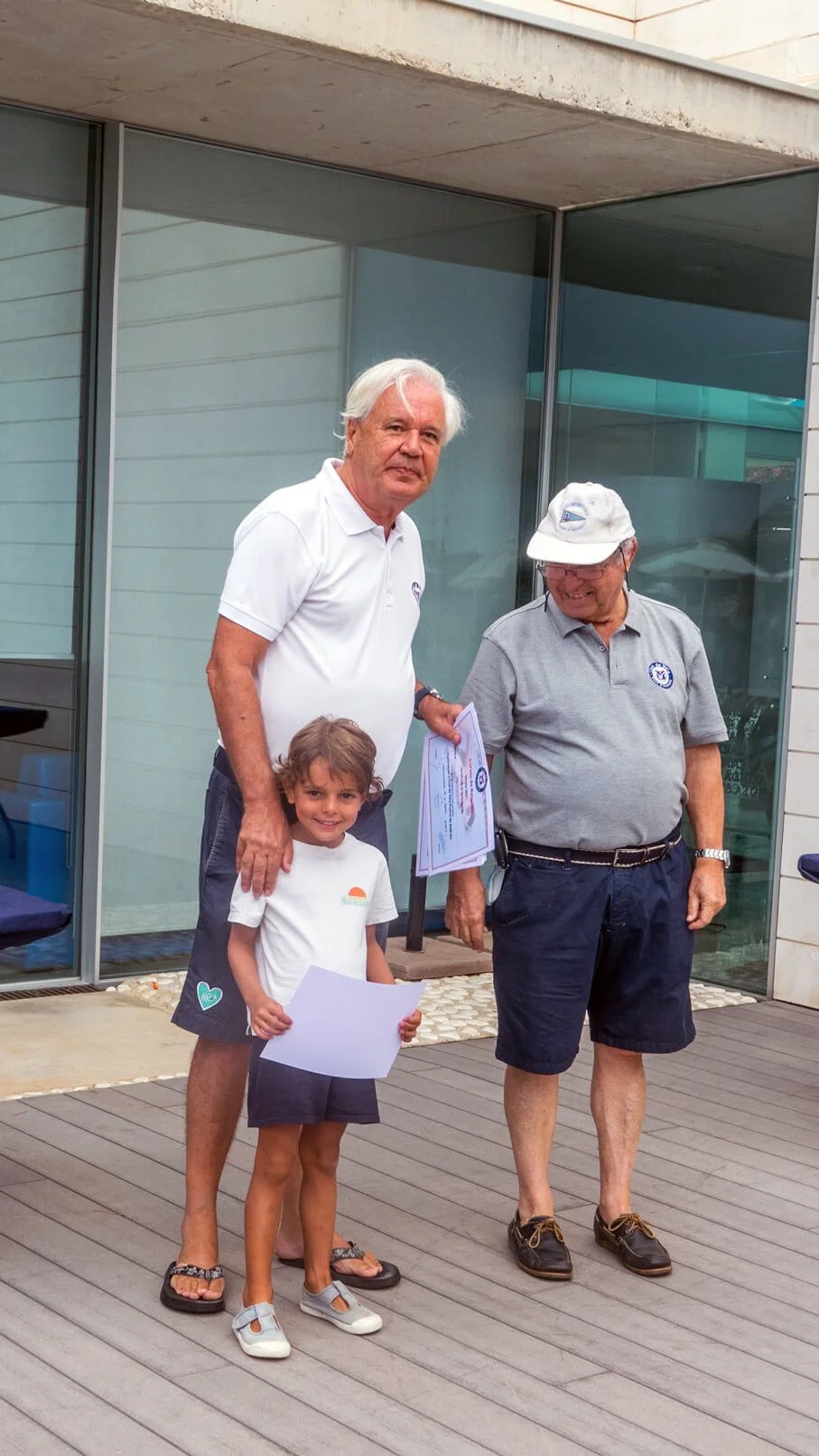 Un grupo de tres personas, incluyendo un niño pequeño, en la entrada de un edificio, con dos hombres adultos entregando certificados.