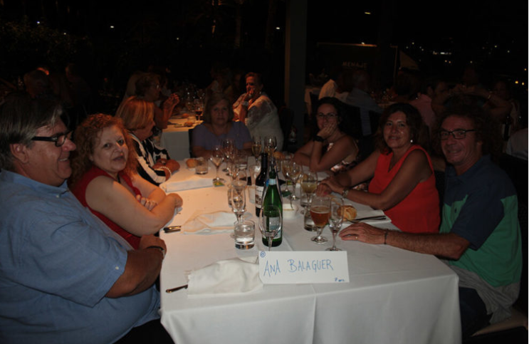 Grupo de personas sentadas en una mesa de restaurante en la noche, con lo que parecen bebidas y comida, en un ambiente elegante y social.