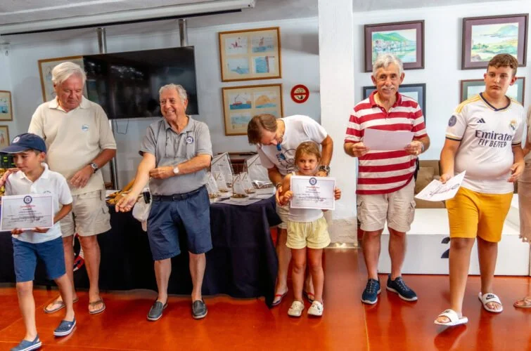 Grupo de personas en una ceremonia de entrega de premios, con niños y adultos sosteniendo certificados, en un ambiente decorado con cuadros en las paredes.