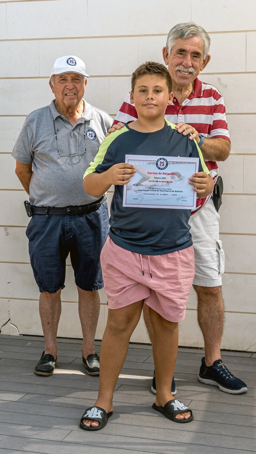 Un niño sosteniendo un certificado de participación en un curso de natación, acompañado por dos adultos que parecen ser entrenadores o instructores, frente a una pared de azulejos.