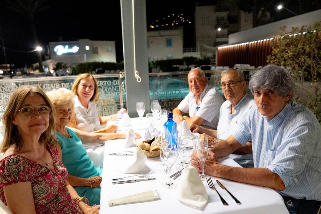 Un grupo de siete personas sentadas en una mesa de restaurante durante la noche, con platos, copas y cubiertos, en un ambiente al aire libre.