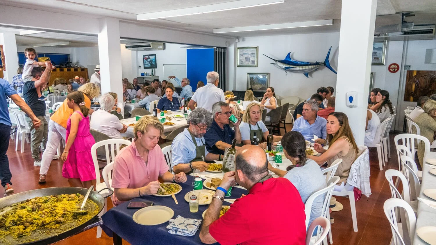 Un grupo de personas sentadas en mesas disfrutando de una comida en un restaurante, con un decorado con peces en las paredes.