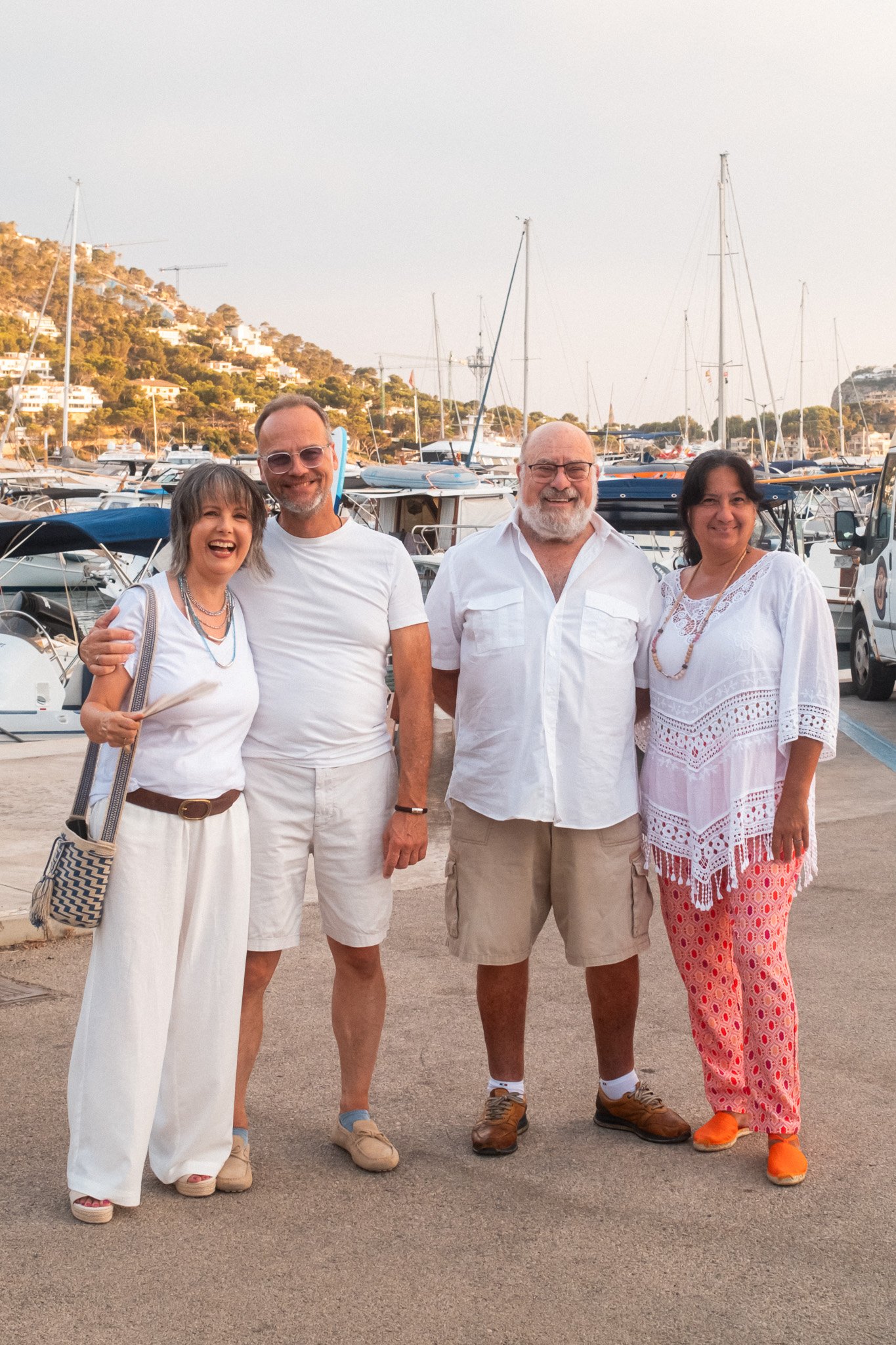 Grupo de cinco personas sonriendo en un muelle con yates y colinas de casas en el fondo, en un día soleado.
