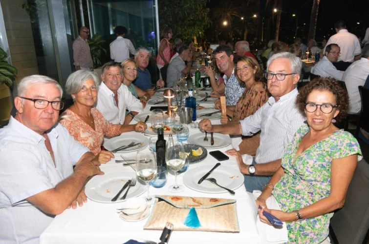 Grupo de personas sentadas alrededor de una mesa larga en un restaurante, disfrutando de una comida en un ambiente elegante con iluminación suave y decoración moderna.