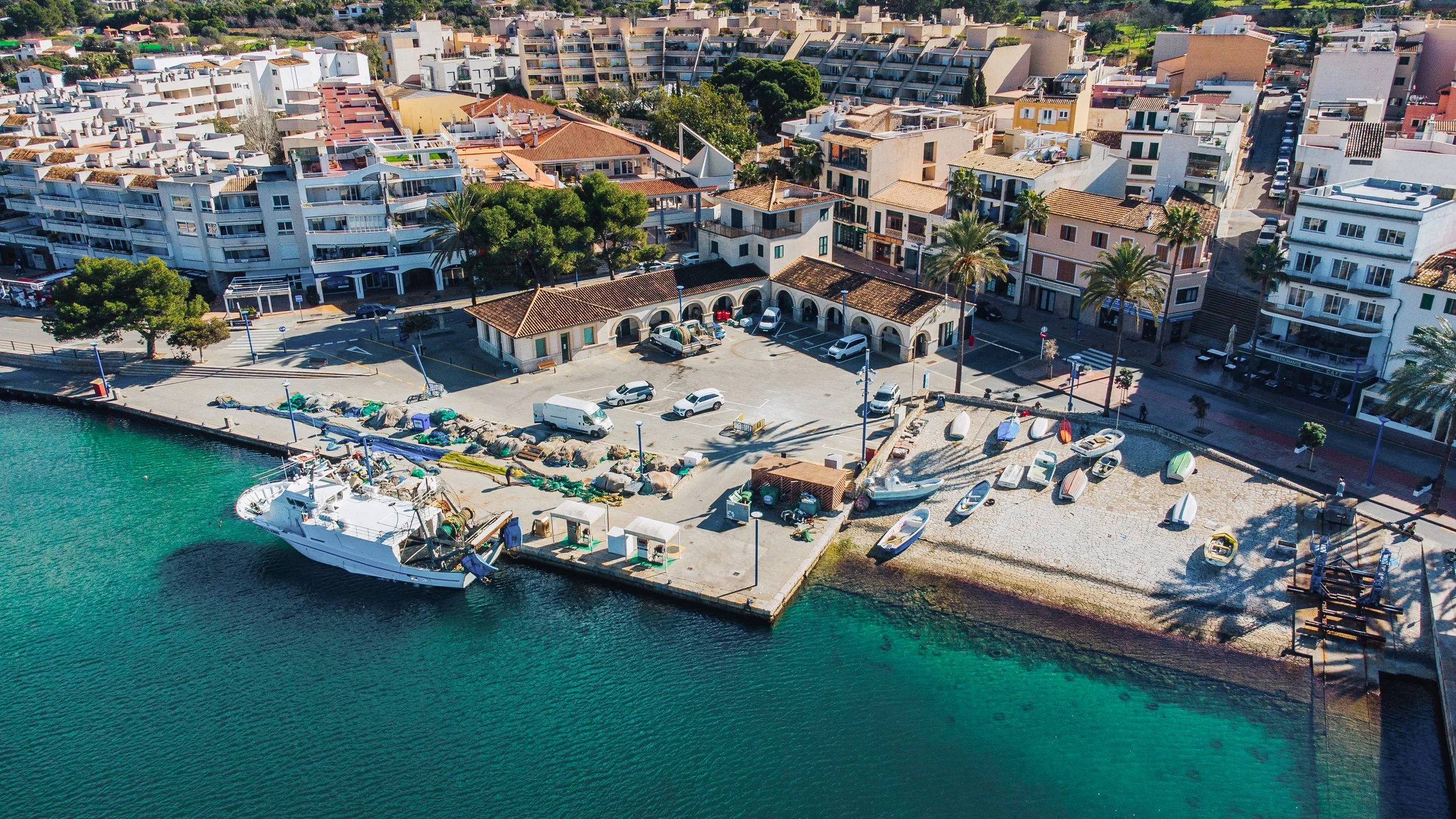 Vista aérea de un puerto con varias embarcaciones y un muelle, rodeado de edificios residenciales y comerciales en una zona urbana junto al agua.