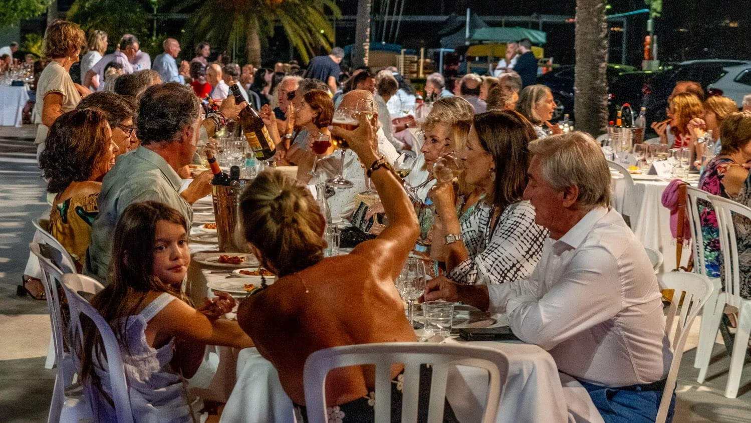 Grupo de personas en una cena al aire libre, brindando y socializando en una mesa larga