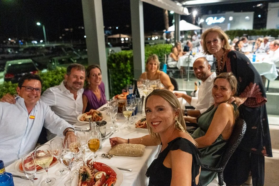 Grupo de personas en una cena al aire libre en la noche, disfrutando comida y bebidas en una mesa larga.