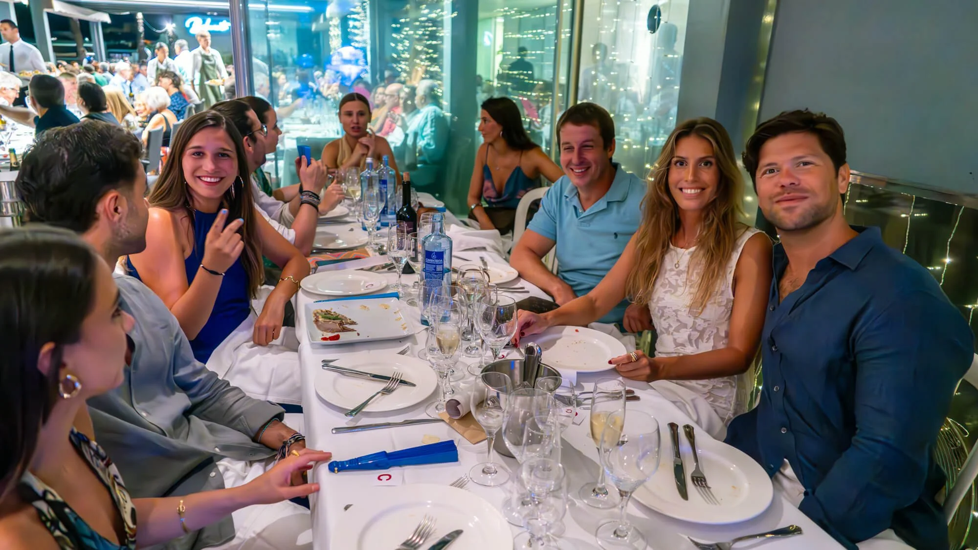 Personas en una cena en un restaurante elegante, sonriendo y disfrutando de la compañía, con varias botellas y copas en la mesa.