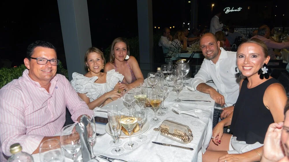 Grupo de seis personas sentadas en una mesa de restaurant elegante, disfrutando de bebidas y convivencia, durante la noche.