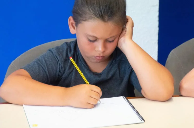 Niña concentrada en dibujar en una hoja de papel en un ambiente escolar.