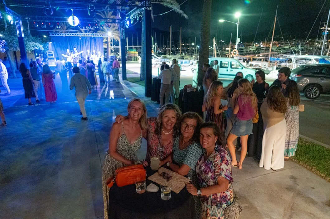 Grupo de personas en una fiesta al aire libre cerca de un puerto, con música en vivo y luces de colores.