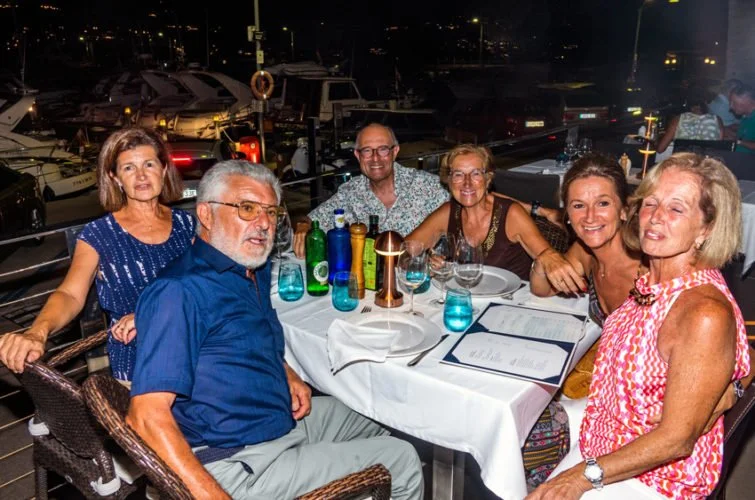 Familia celebrando en un restaurante junto al puerto, comiendo y disfrutando de la noche.