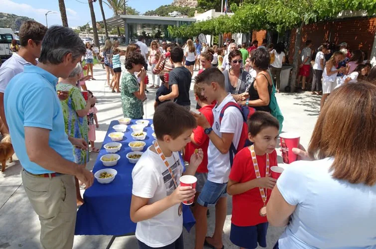 Niños y adultos en fila recibiendo comida en una fiesta al aire libre.