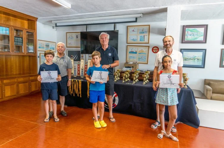Niños y adultos en una ceremonia de premiación, sosteniendo certificados y trofeos, en un ambiente decorado con cuadros y exhibiciones en la pared.