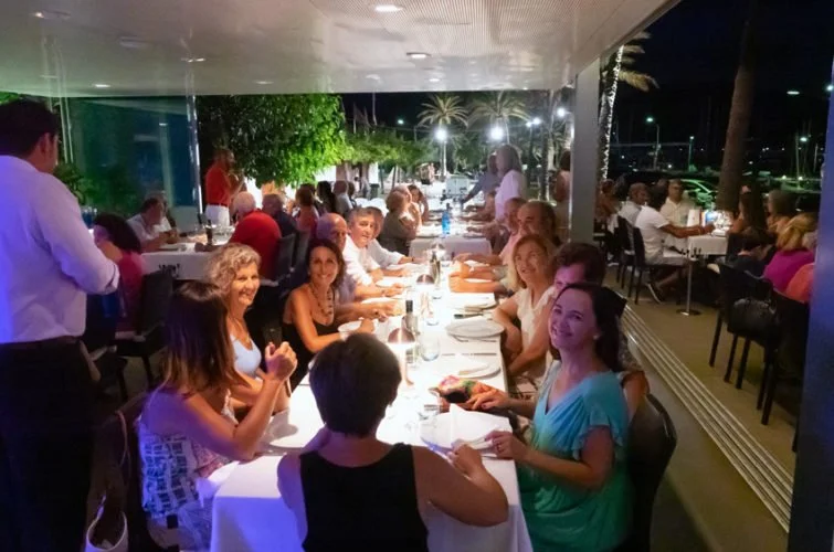 Grupo de personas sentadas en una mesa larga en un restaurante al aire libre por la noche, celebrando una comida o cena.