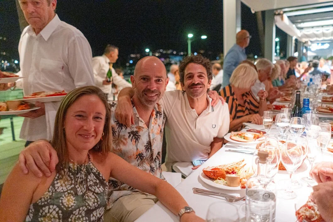 Grupo de personas en una cena al aire libre en la noche, sonriendo y disfrutando de la comida.