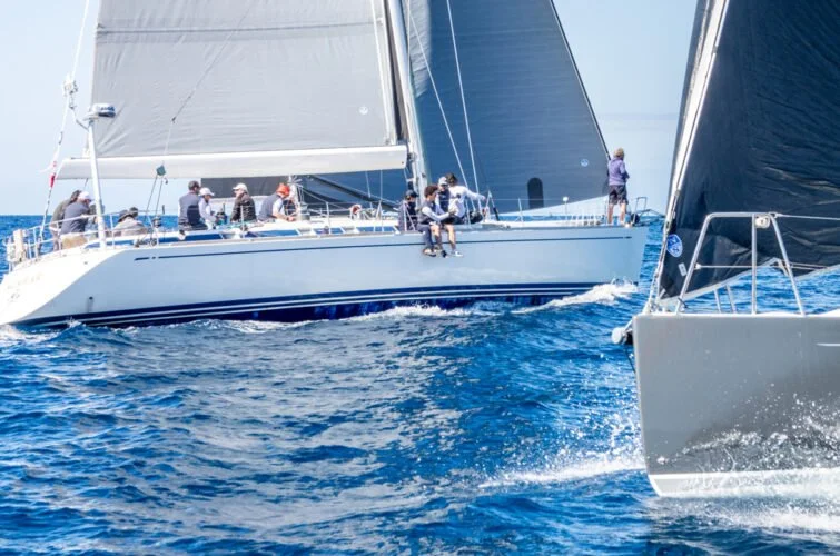 Barco de vela con varias personas navegando en el mar, vista lateral del velero y el agua azul.