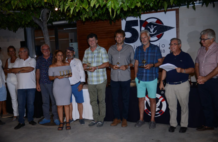 Grupo de personas en una ceremonia de premiación, con un fondo que muestra un logo y la celebración del 50 aniversario en un ambiente al aire libre.