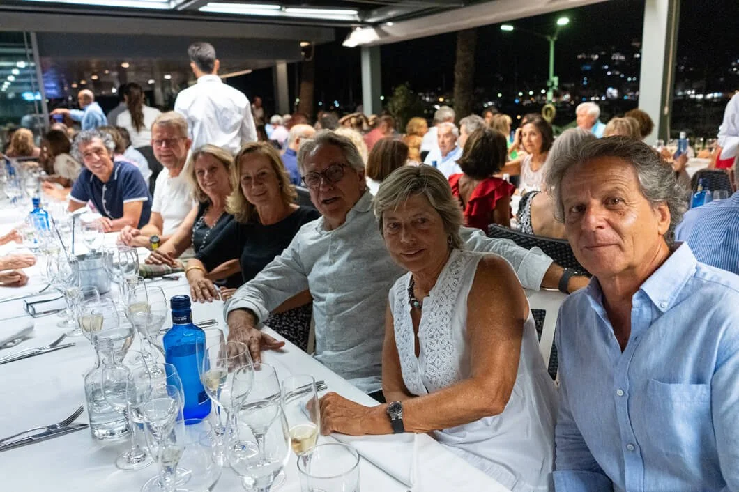 Grupo de personas sentadas en una mesa de comida en un restaurante durante la noche, con muchas copas y botellas sobre la mesa.