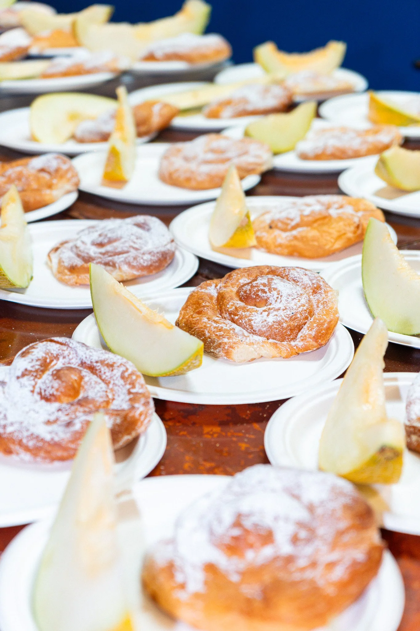 Diverse pasteles de crema en platos blancos con rodajas de melón y limón de acompañamiento.