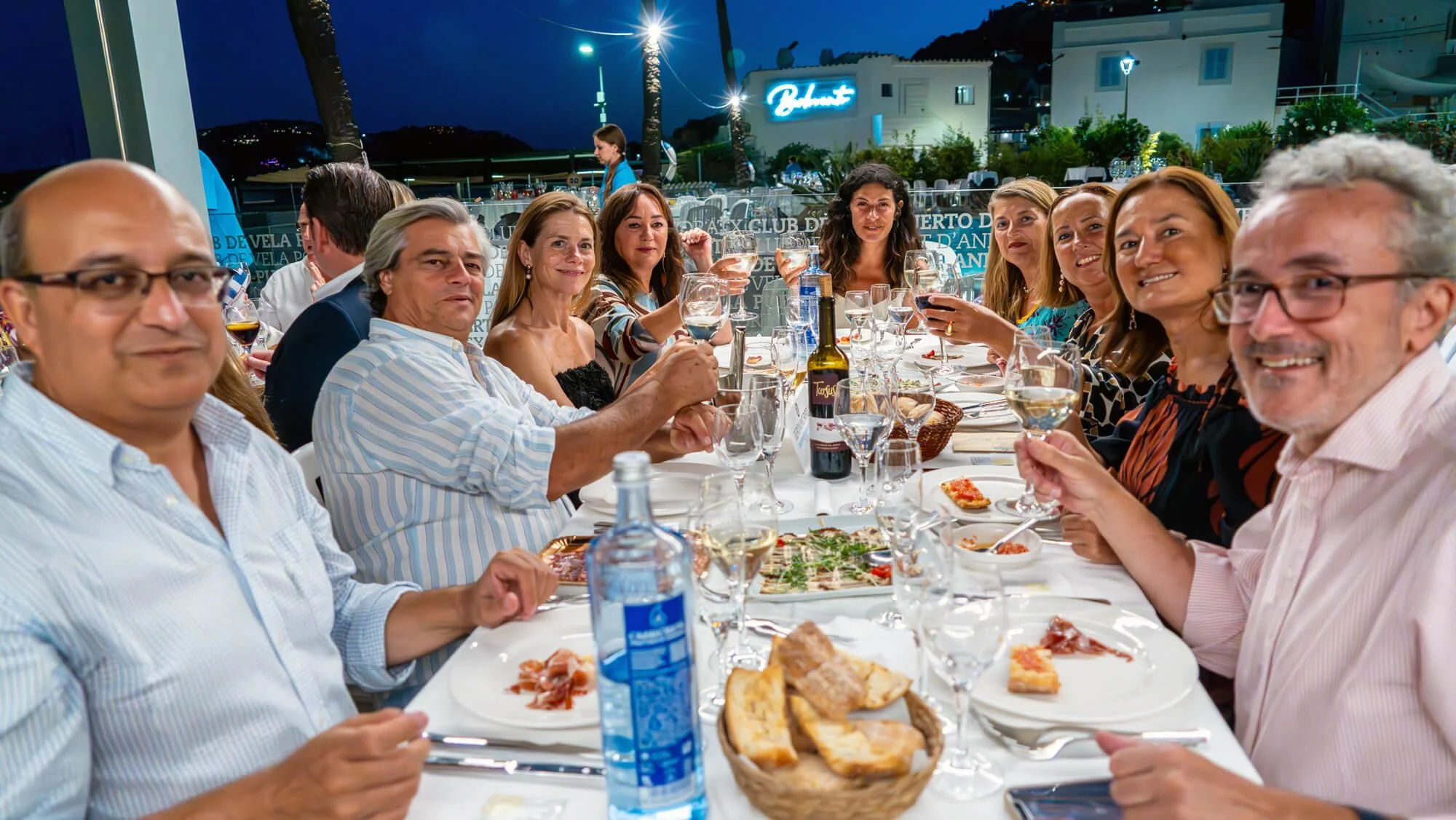 Grupo de personas disfrutando de una cena en un restaurante en la terraza durante la noche, con comida, bebidas y conversación.