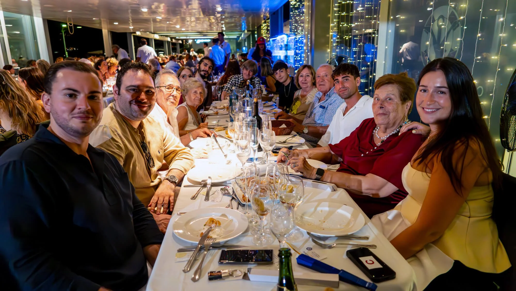 Grupo de personas sentadas en una mesa durante una cena en un restaurante elegante, con decoración de luces y un ambiente festivo.