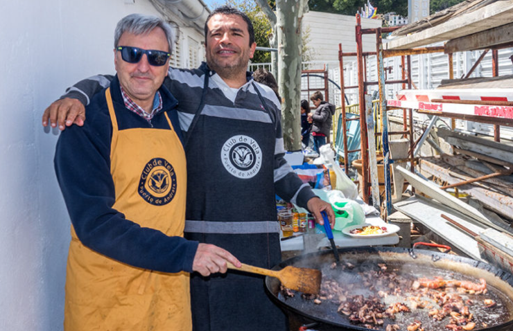 Dos hombres cocinando carne en una parrilla en un evento al aire libre.