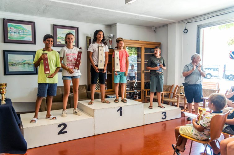 Niños en un podio de premios en una ceremonia de premiación, con adultos y niños observando.