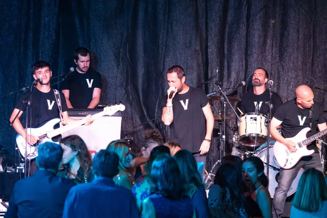 Una banda musical tocando en un escenario con público disfrutando del concierto.