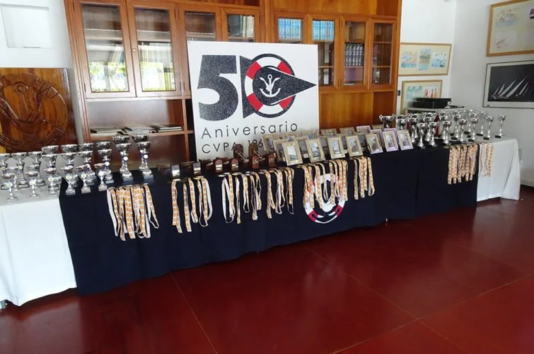 Mesa decorada con trofeos, premios y fotografías, con un cartel que celebra el 50 aniversario de la asociación CVPR.