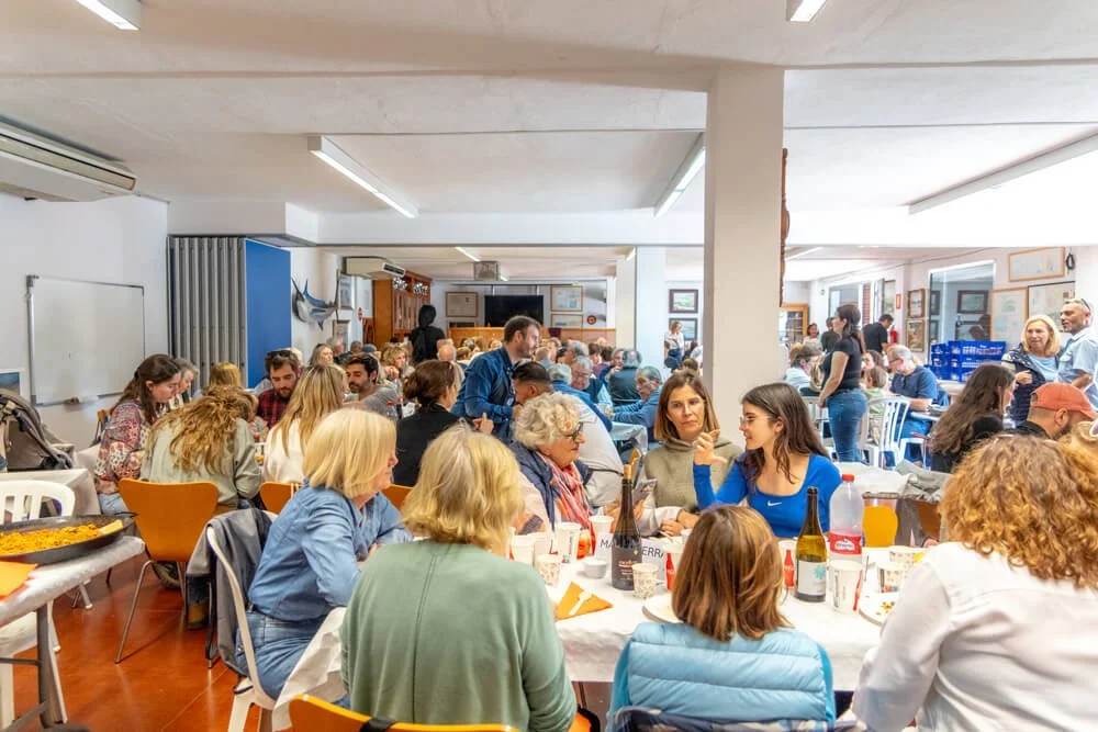 Gente en una reunión social en un comedor con mesas llenas y varias personas conversando