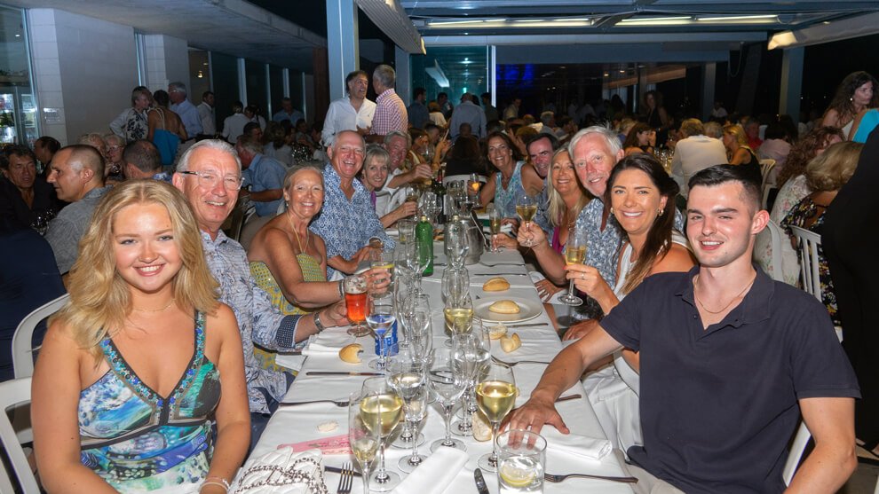 Grupo de personas sentadas en una mesa durante una celebración o comida en un restaurante, sonriendo y brindando.