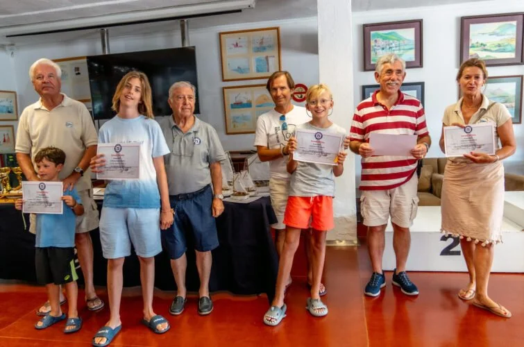 Grupo de personas en una ceremonia de premiación, sosteniendo diplomas y trofeos, en un ambiente con cuadros en las paredes.