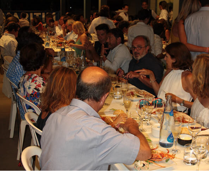 Grupo de personas cenando en una larga mesa en un restaurante, conversando y disfrutando de la comida.