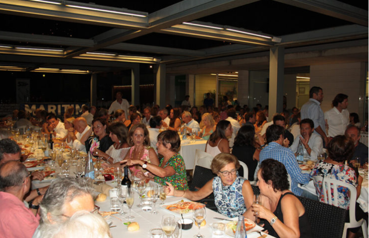 Personas cenando en un restaurante con muchas mesas y comensales en un ambiente cerrado y bien iluminado.