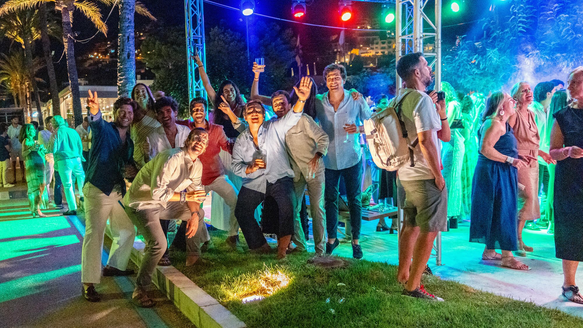 Grupo de personas bailando y sonriendo en una fiesta al aire libre con iluminación colorida