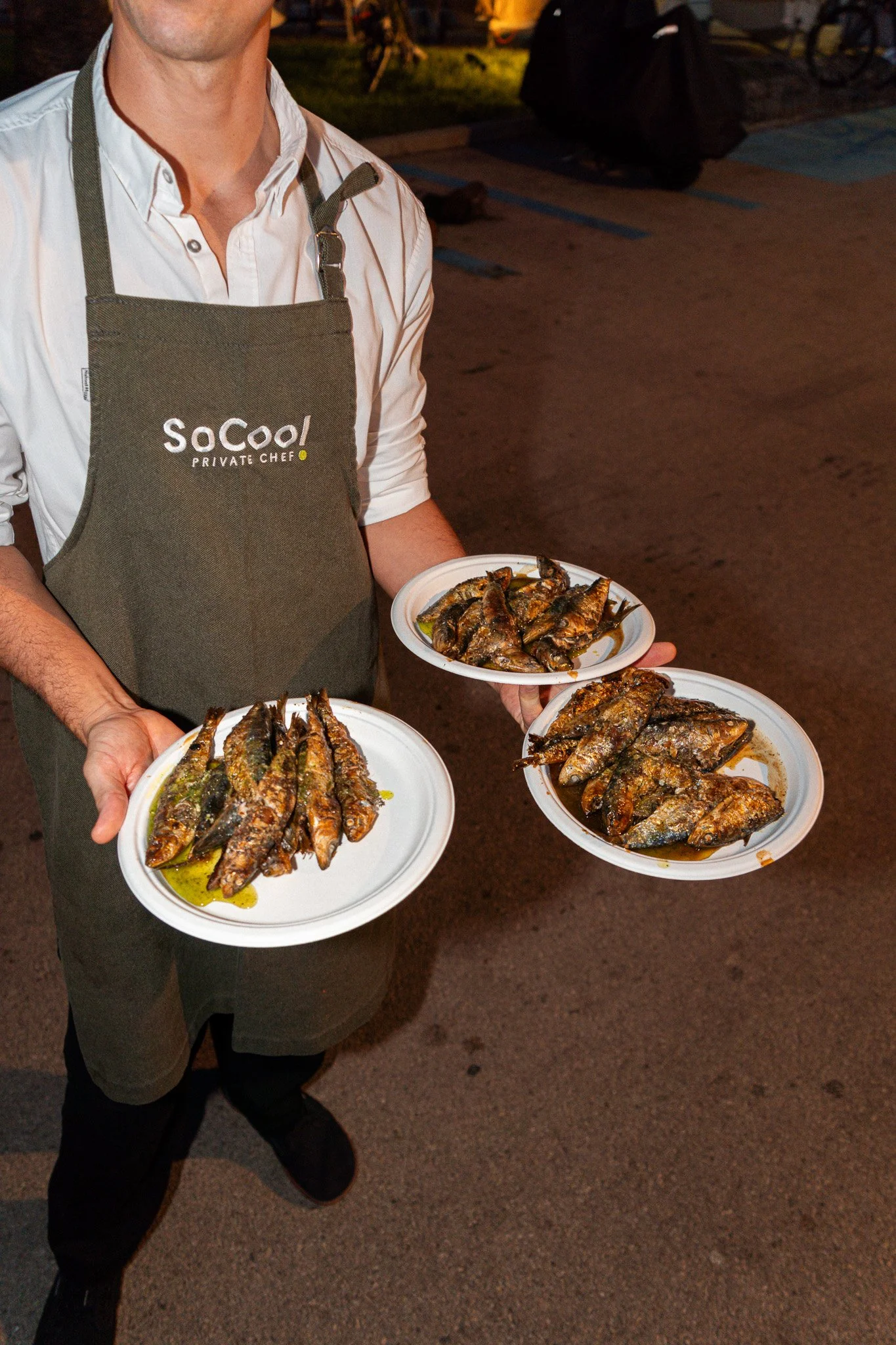 Persona sosteniendo tres platos con sardinas fritas en un entorno nocturno.