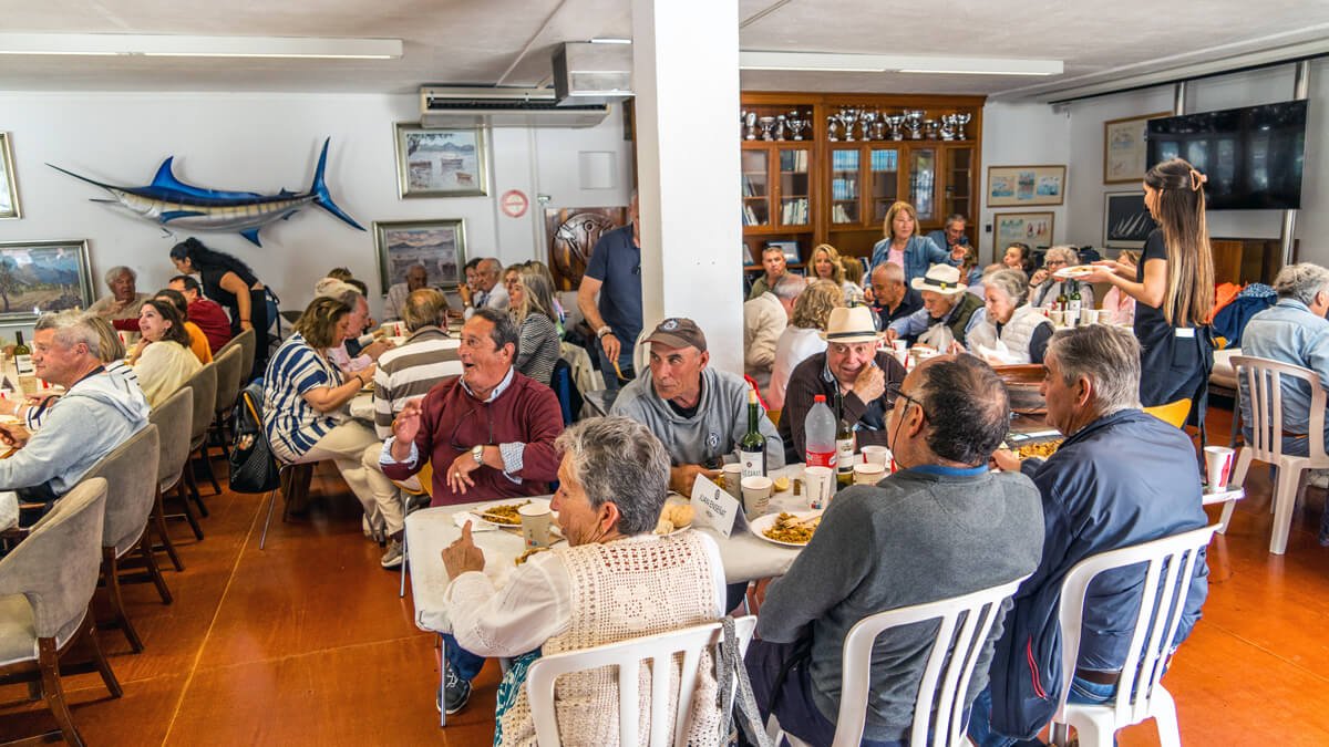 Personas en un comedor disfrutando una comida en un ambiente social, con decoración náutica en las paredes y un televisor grande en la esquina.