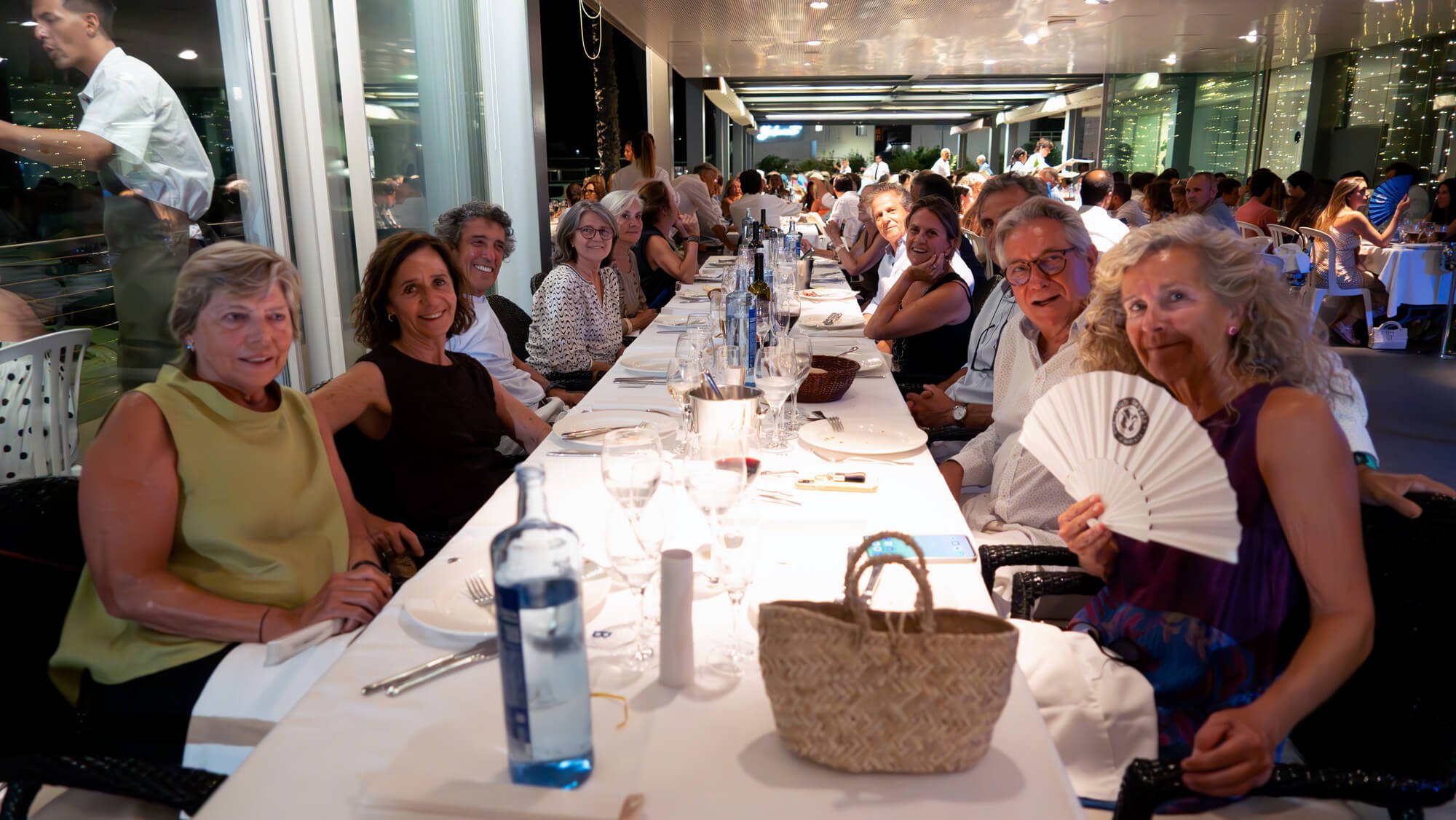 Personas sentadas a una mesa en un restaurante elegante por la noche, sonríen y parecen disfrutar de una cena social.