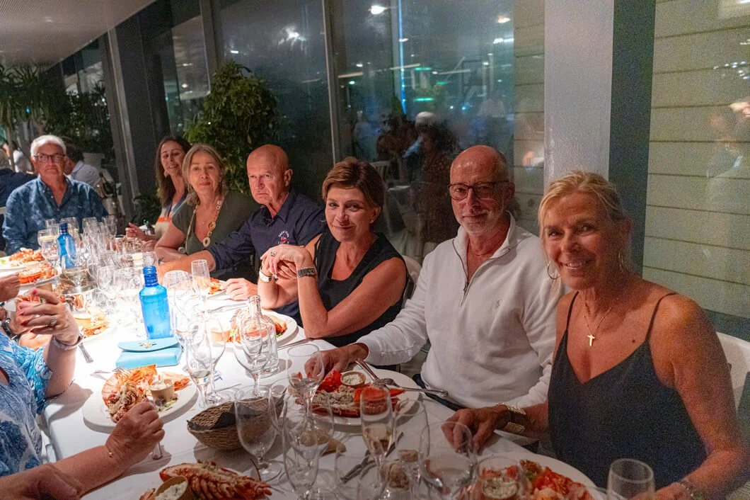 Grupo de personas sentadas en una mesa en un restaurante, disfrutando de una comida, con platos de mariscos, copas y bebidas, en un ambiente elegante y moderno.