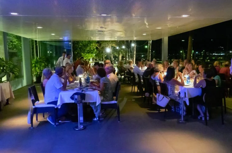 Grupo de personas cenas en un restaurante al aire libre por la noche, con decoración luminosa y mucho verde alrededor.