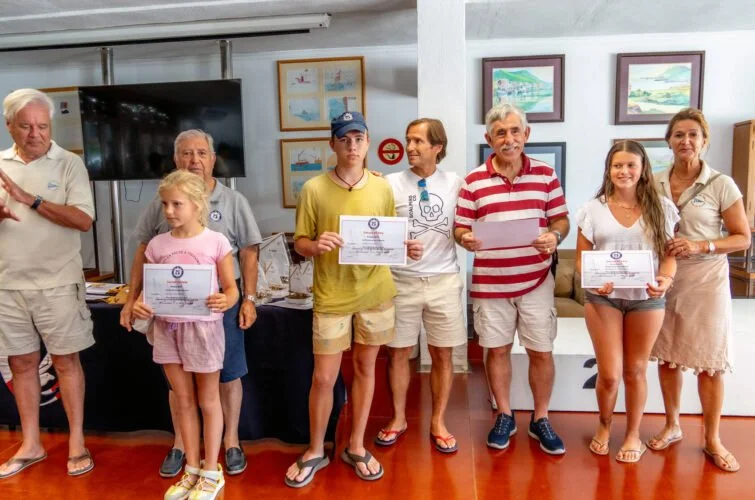 Un grupo de personas, incluyendo niños y adultos, sosteniendo certificados en un salón con pinturas en las paredes, parecen estar en una ceremonia de premiación o reconocimiento.