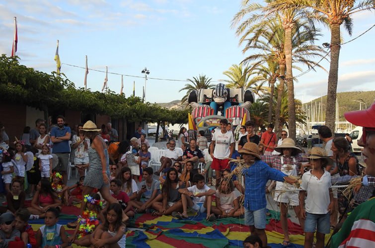 Personas y niños en una fiesta al aire libre con decoraciones, palmeras y una máquina de algodones en el fondo.