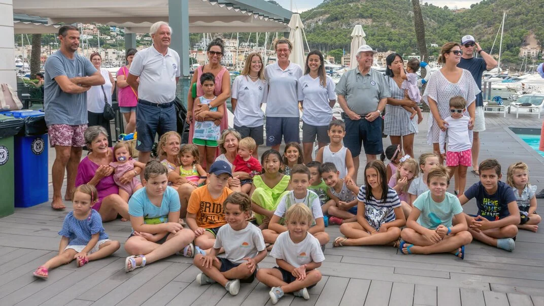Grupo de niños y adultos en un muelle cerca del agua y yates, en un día soleado, posando para la foto.