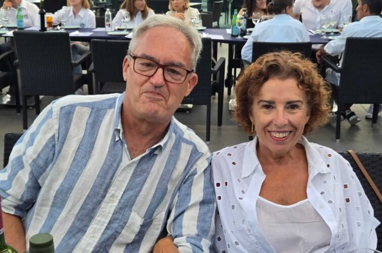 Un hombre y una mujer sentados en una mesa en un restaurante o cafetería, rodeados de otras mesas con comensales.