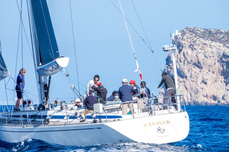 Varias personas navegando en un velero en el mar con rocas en el fondo.