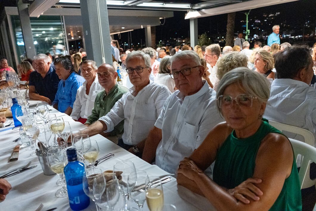 Grupo de personas sentadas en una mesa en un evento social en un restaurante cubierto durante la noche, algunos con bebidas y comida en la mesa.